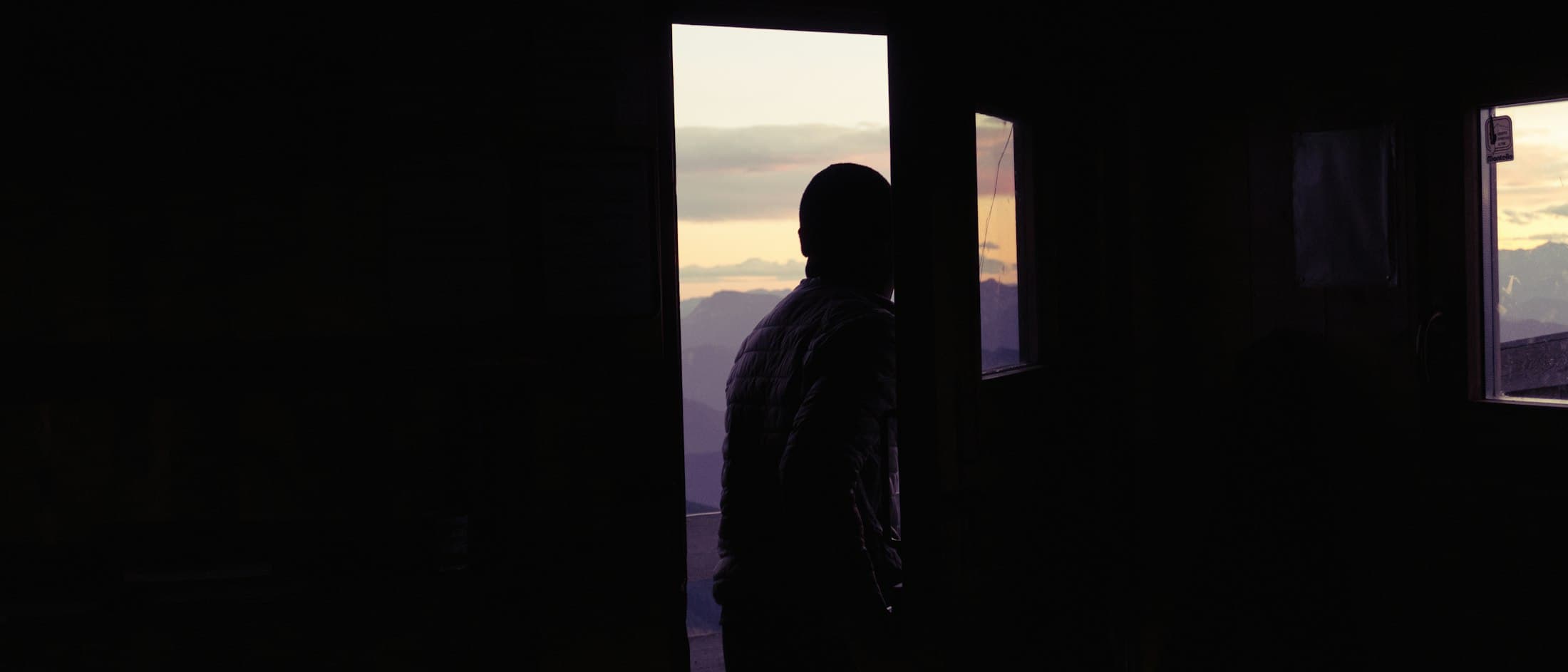 Pessoa observando montanhas ao pôr do sol através de uma grande janela